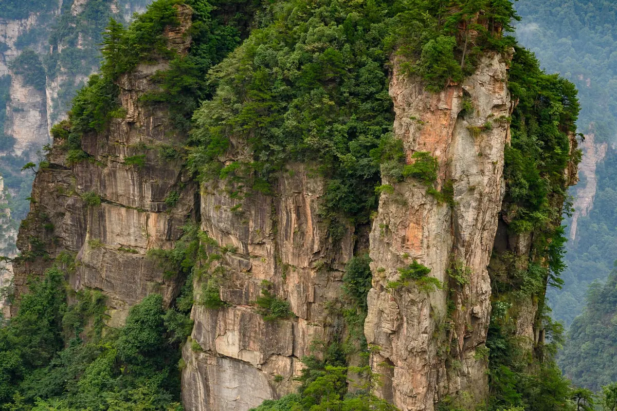 Sheer sandstone cliff faces covered with patches of green vegetation in Zhangjiajie