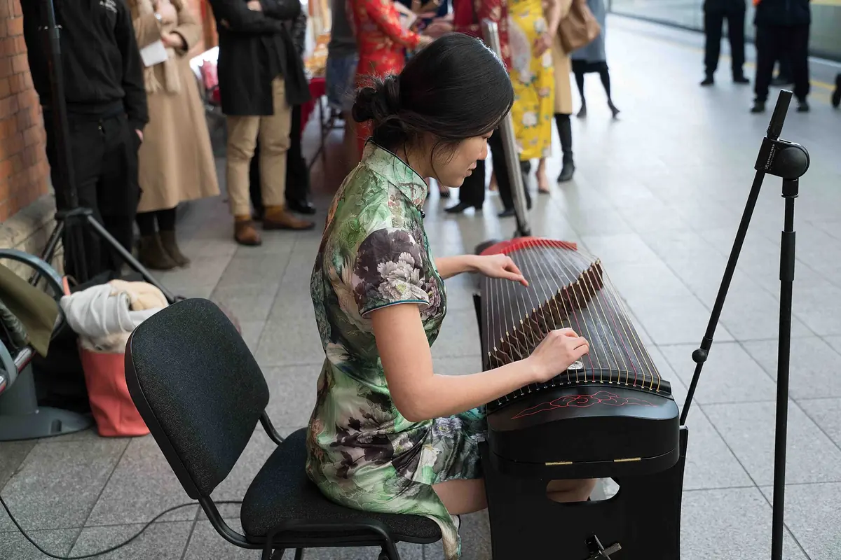 Frau im Blumenmusterkleid spielt neben einem Mikrofon Guzheng