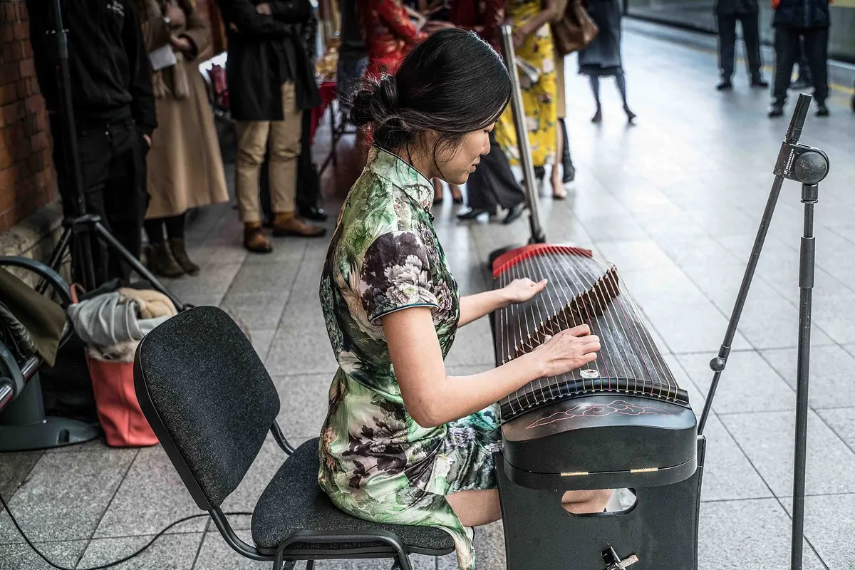 Guzheng player performing for a small audience on a station platform