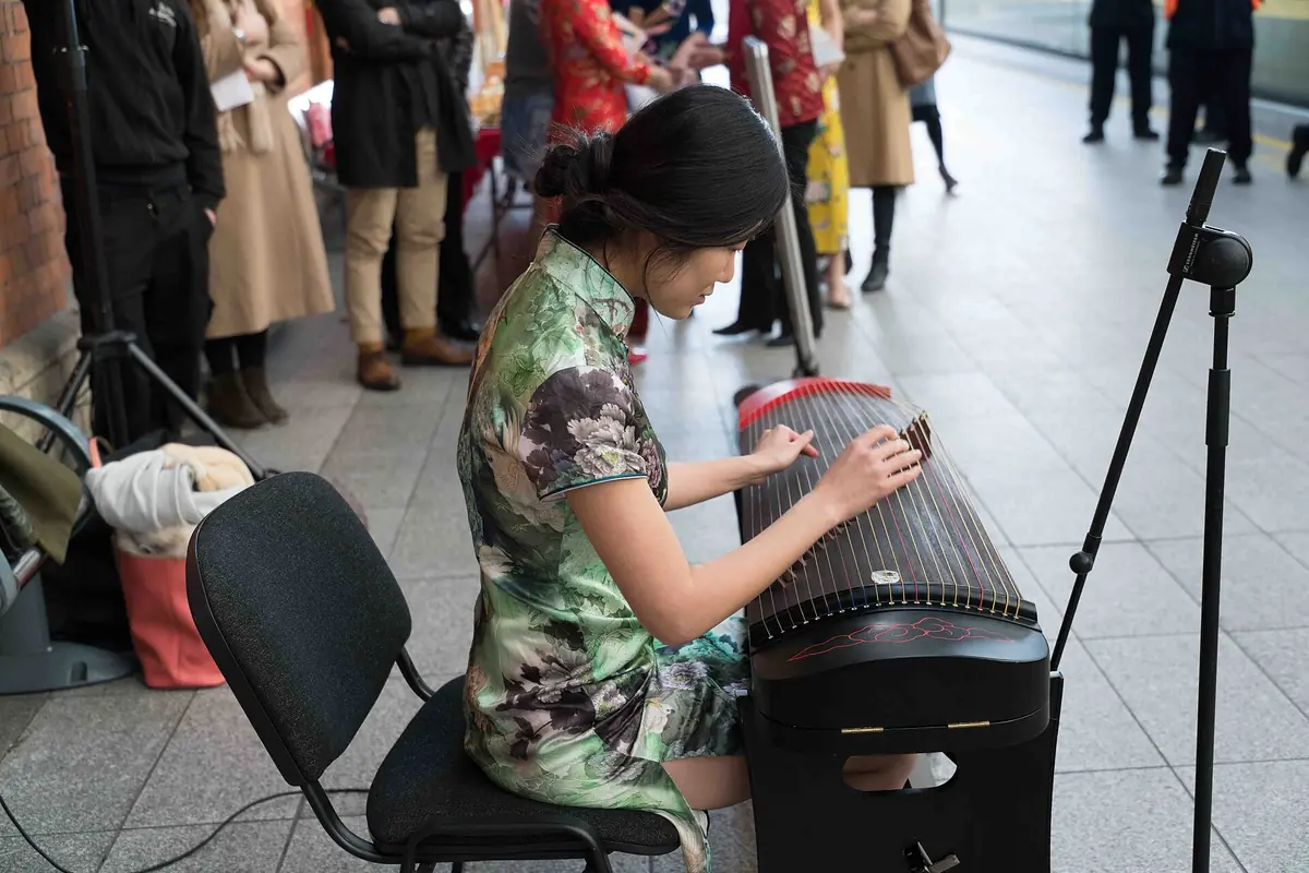 Seated woman plucking the strings of a guzheng with a microphone nearby