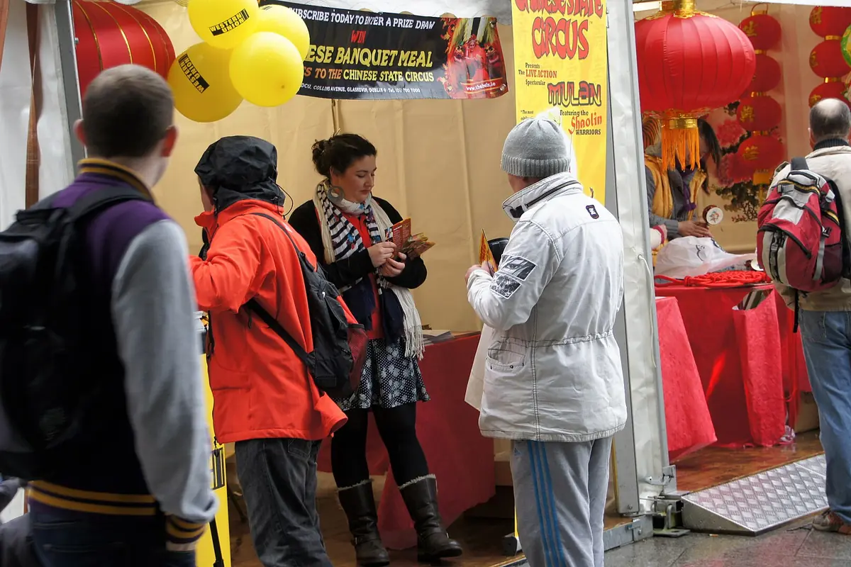 Visitors talking beside a red festival stall decorated with yellow lanterns