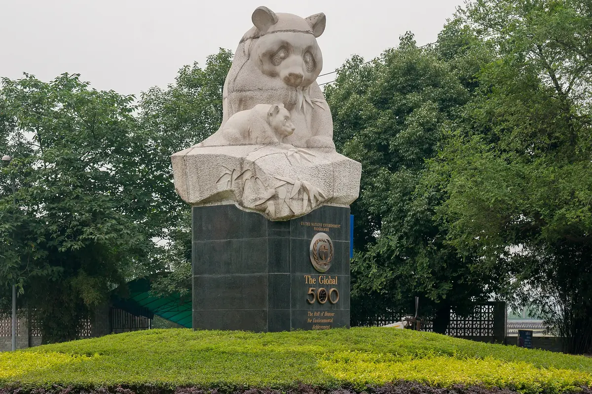 Stone panda sculpture on a pedestal among trees and a trimmed green lawn