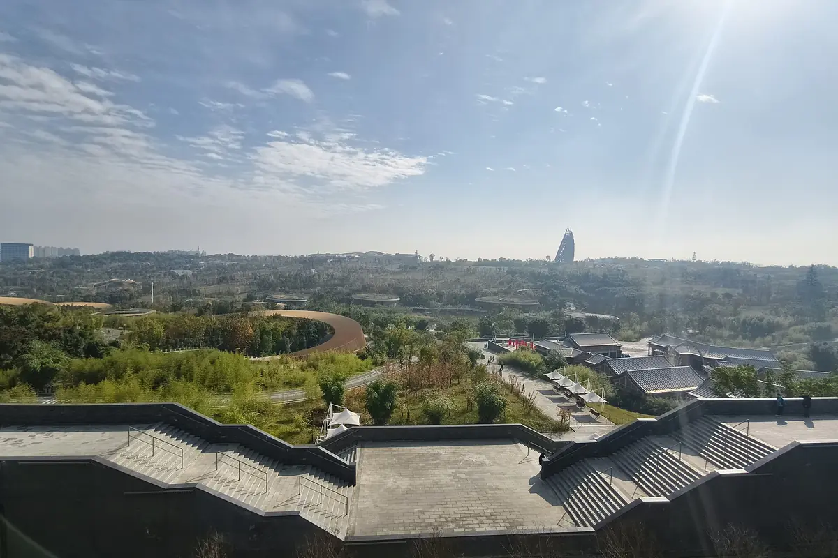 Dark tiled rooftops overlooking a green park and distant city beneath scattered clouds