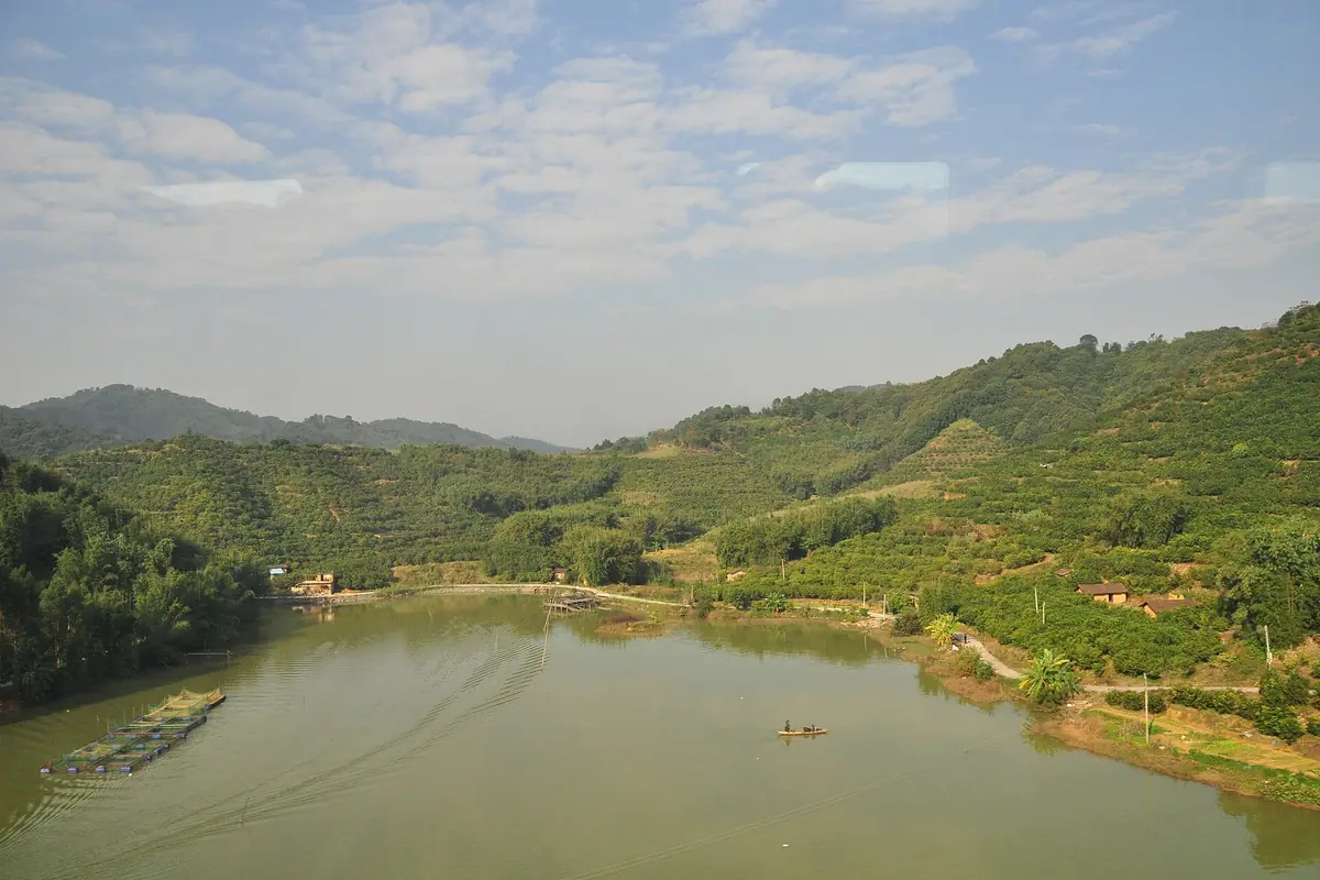 Wooded hills and scattered buildings beside a quiet lake in the Guangzhou area