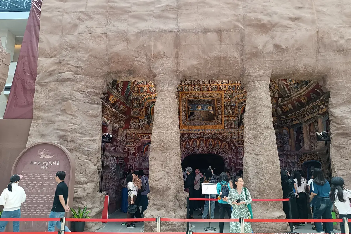 Visitors outside cave entrances with colorful murals inside a pale earthen facade