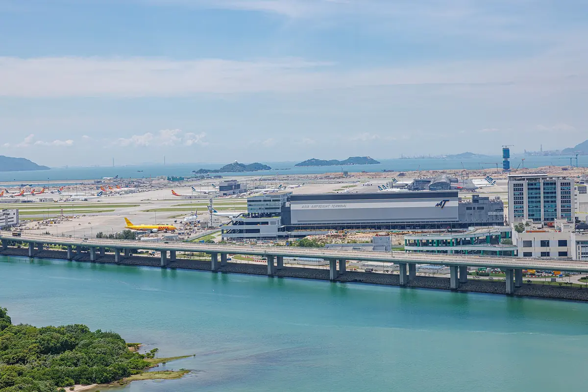 Airport terminal and elevated roadway beside coastal water under a pale sky