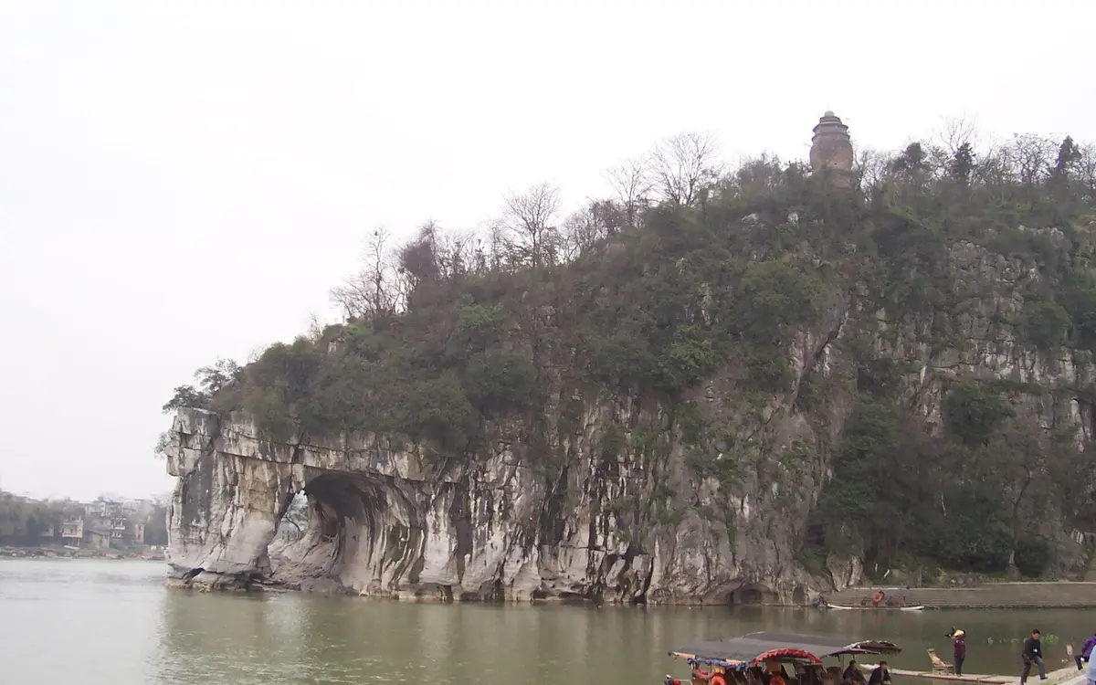 Sheer limestone hill covered with trees beside a calm river in Guilin
