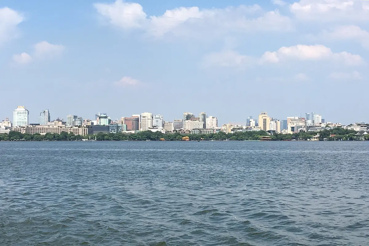 Wide blue lake beneath a distant city skyline and pale clouds