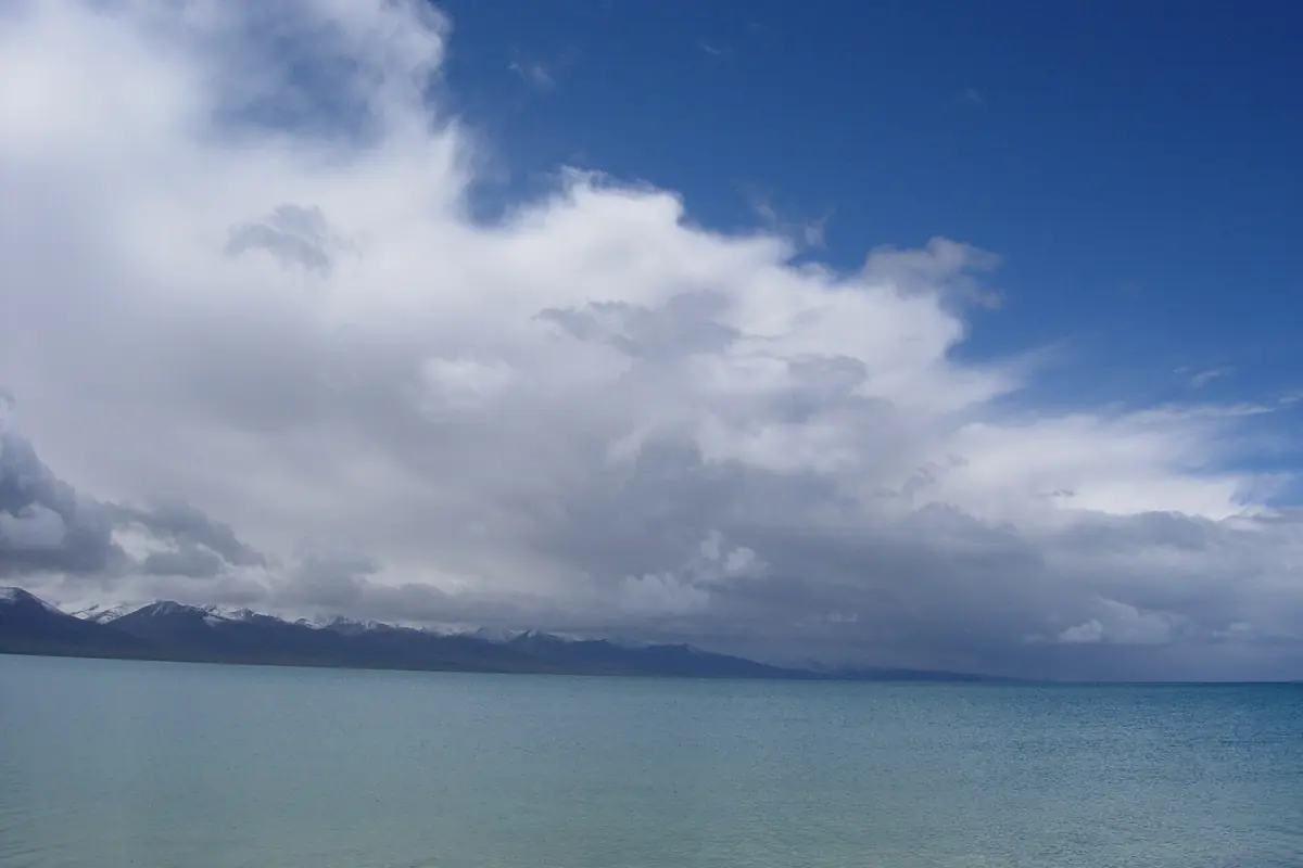 Turquoise lake beneath distant dark mountains and broad white clouds