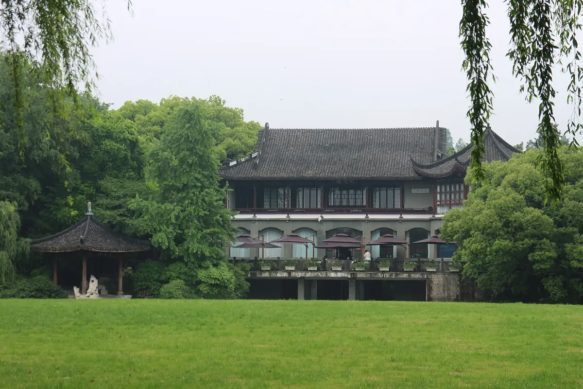 Traditionelles Gebäude mit dunklem Dach hinter einer grünen Rasenfläche und Weiden