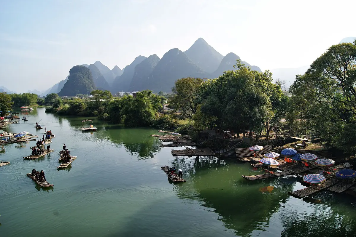 Small boats on a calm river beneath trees and distant karst peaks