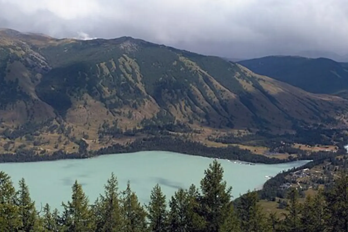 Tasik gunung biru kehijauan pucat bersempadan dengan pokok konifer gelap dan cerun berbatu