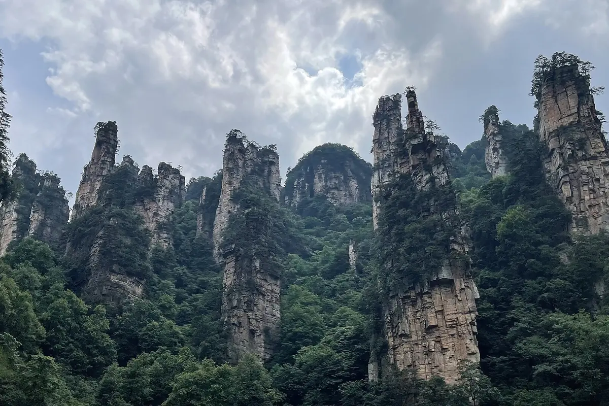 Tiang batu pasir tinggi yang dilitupi hutan di bawah langit mendung di Zhangjiajie
