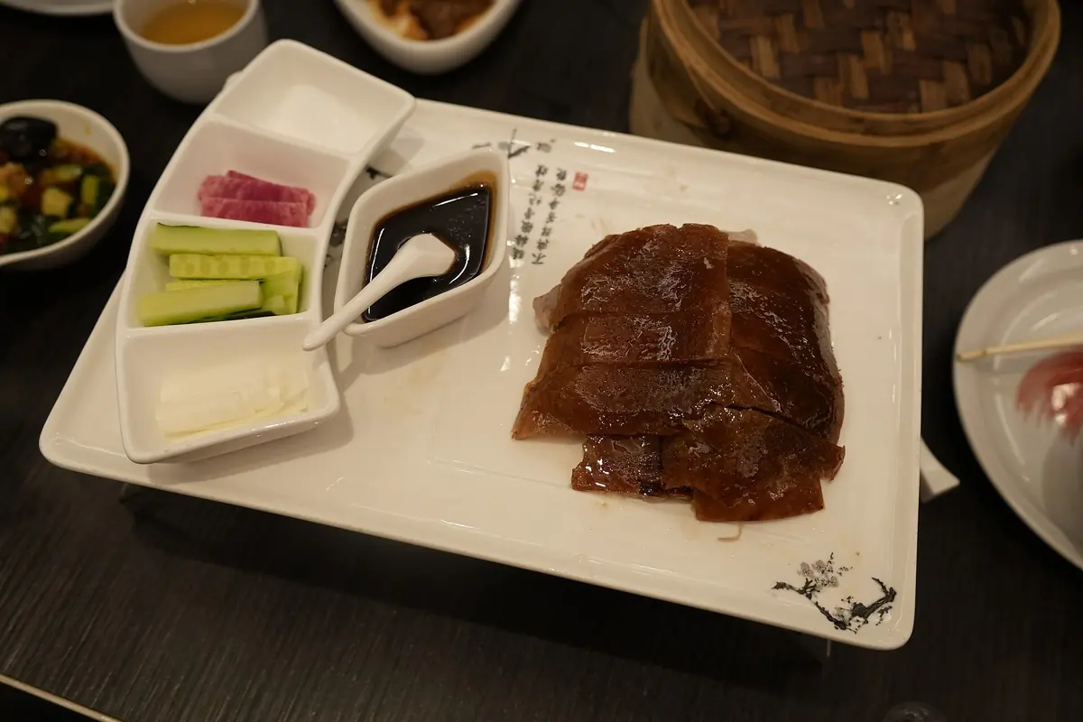 Canard rôti tranché avec galettes, concombre et sauces sur un plat de service blanc