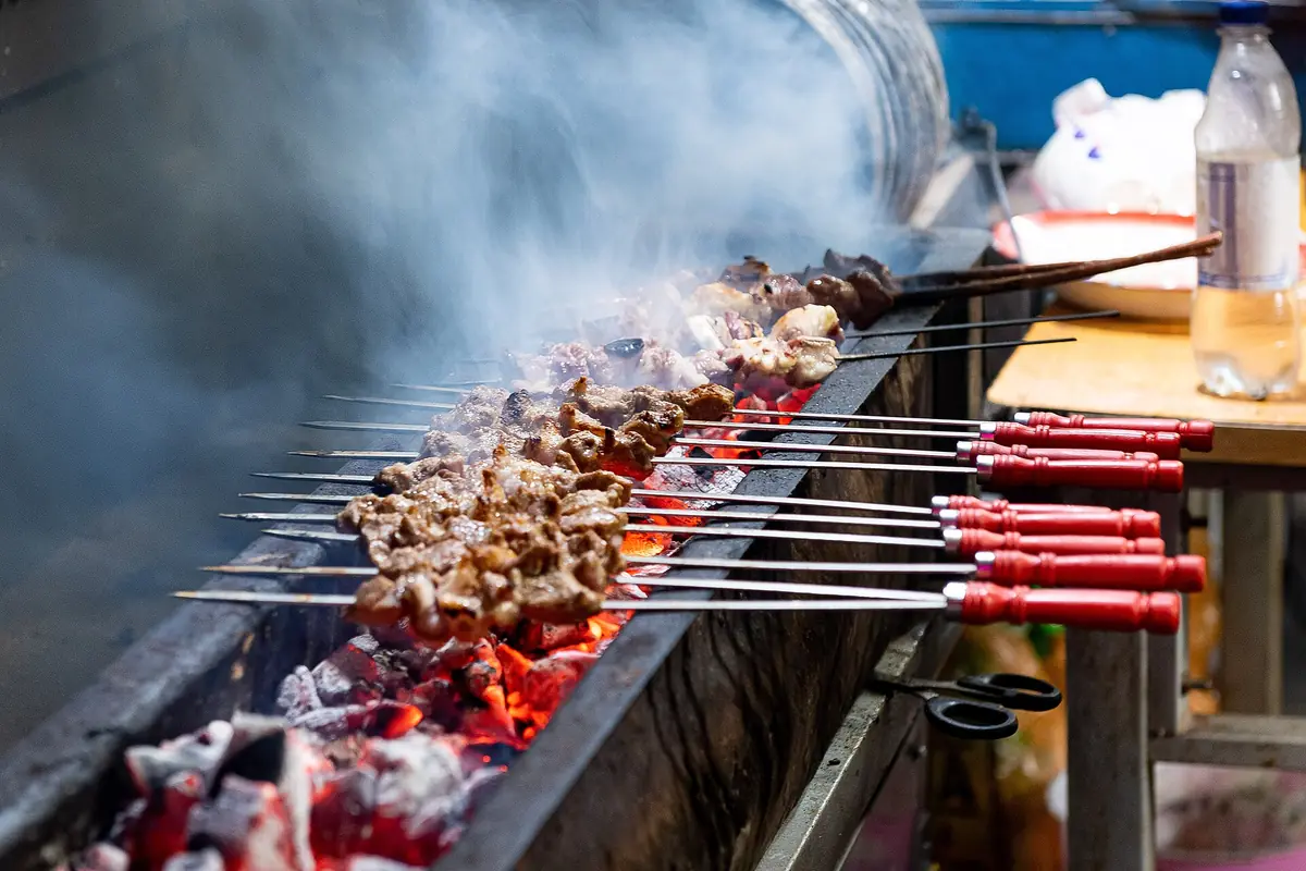 Meat skewers grilling above glowing coals with smoke rising from the barbecue