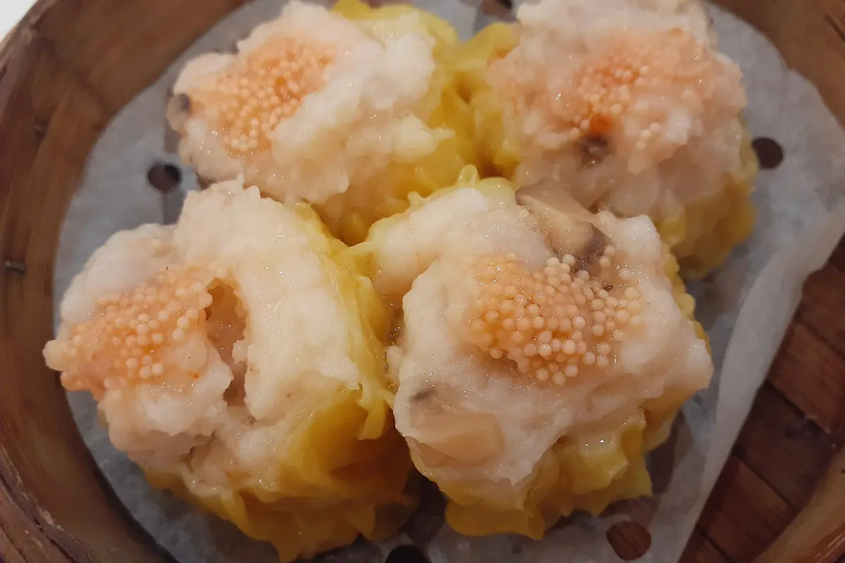 Raviolis shumai jaunes garnis d’œufs de poisson orange dans un panier vapeur en bambou