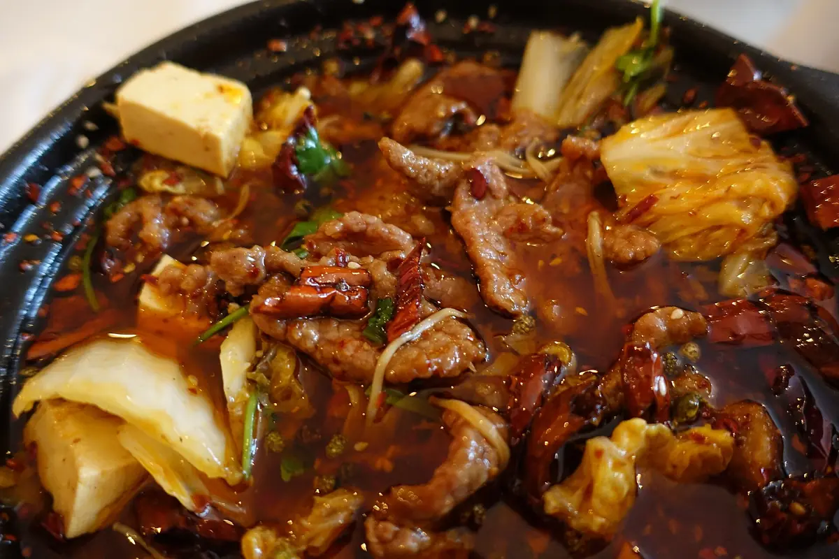 Ragoût rouge au piment, tofu, viande et légumes verts dans un plat de service noir
