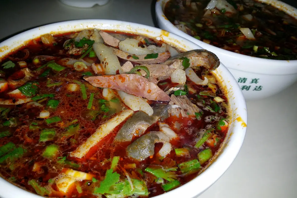 Bowls of red chili broth with sliced meat and chopped green herbs
