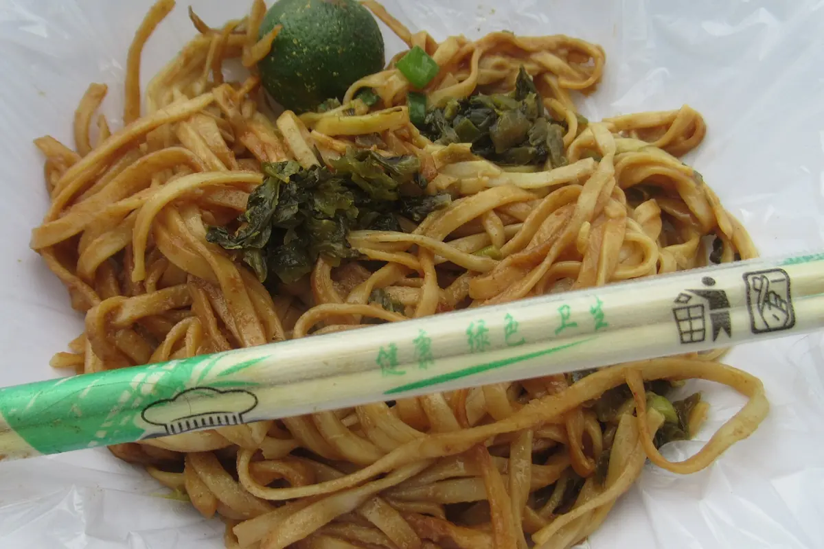 Nouilles sautées aux légumes verts avec des baguettes emballées sur une assiette blanche