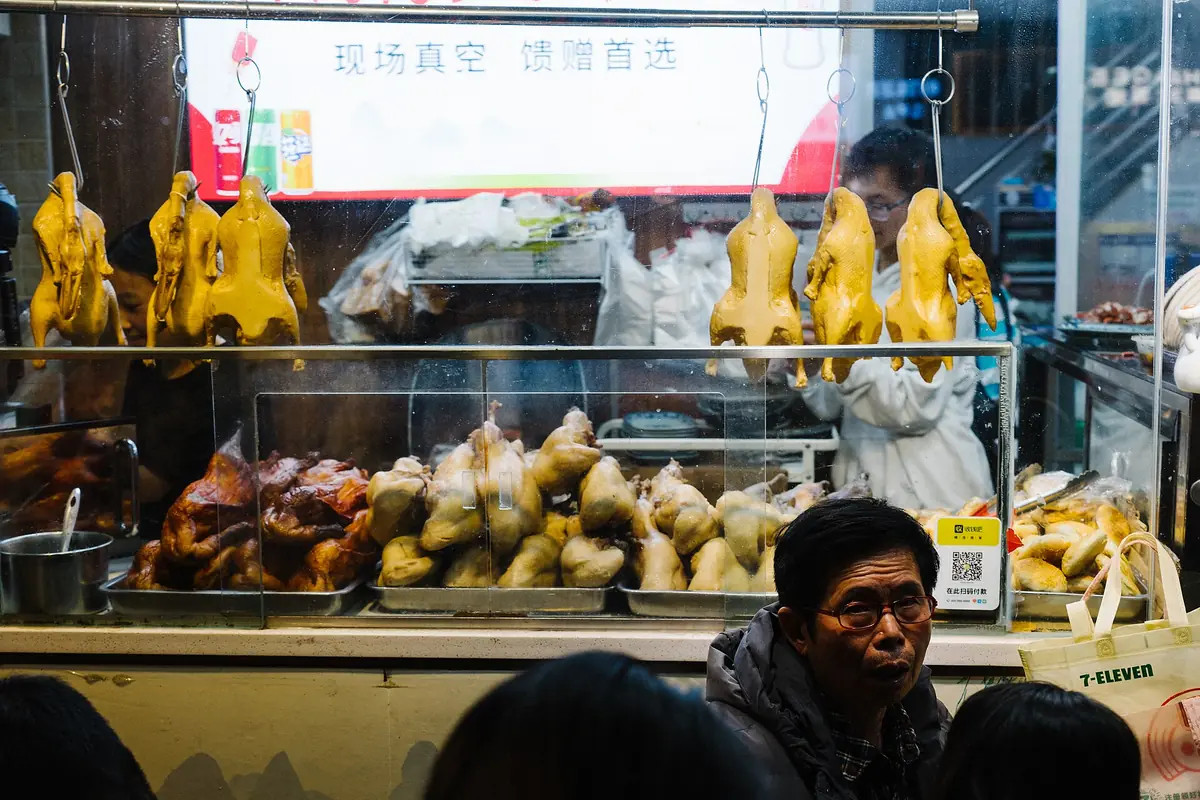 Cooked poultry hanging above a food-shop counter beside seated customers