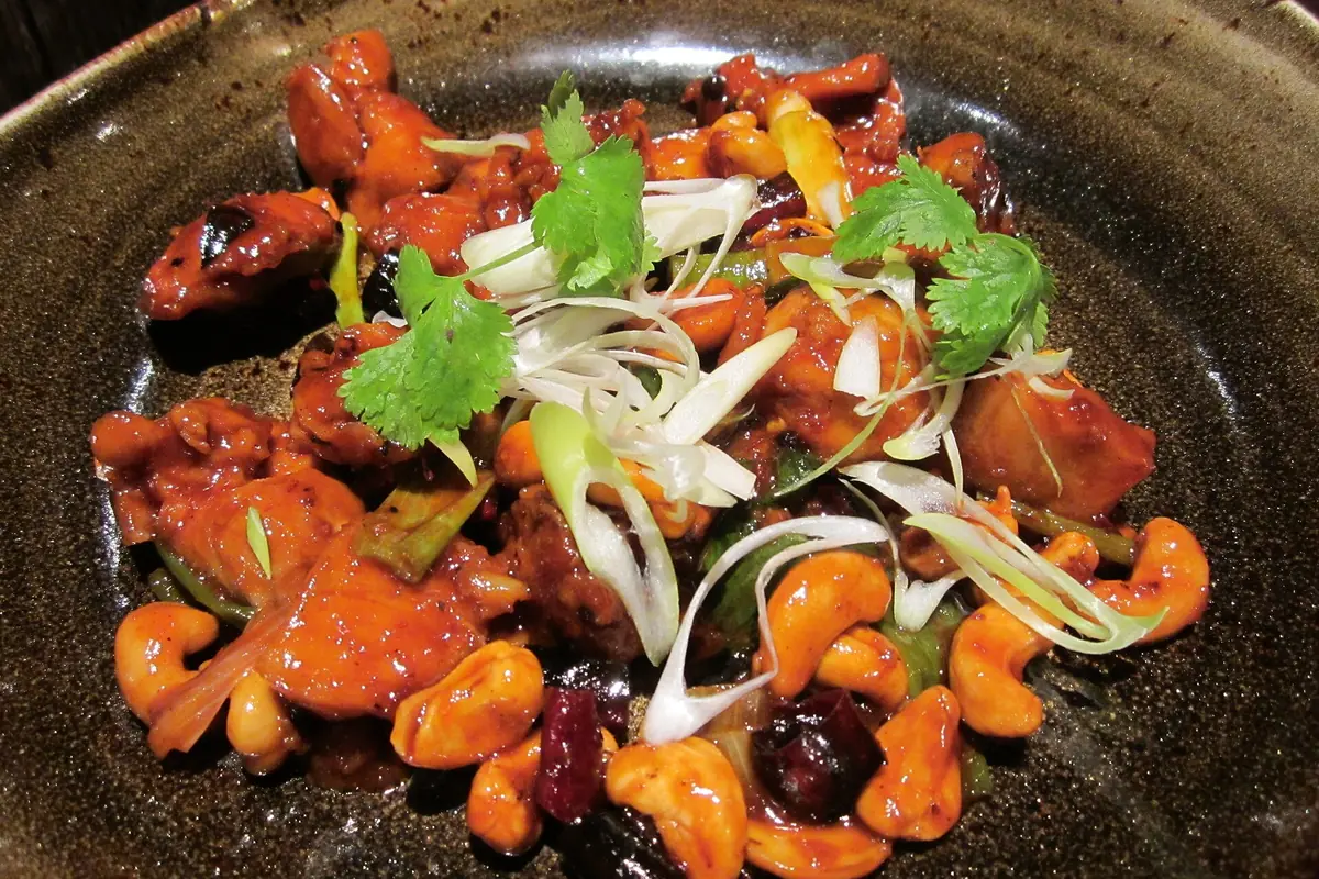 Red chili-covered stir-fry topped with sliced onions and cilantro in a black bowl