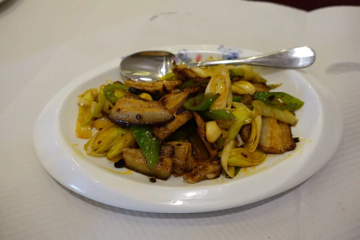 Stir-fried sliced vegetables and meat on a white plate with a metal spoon