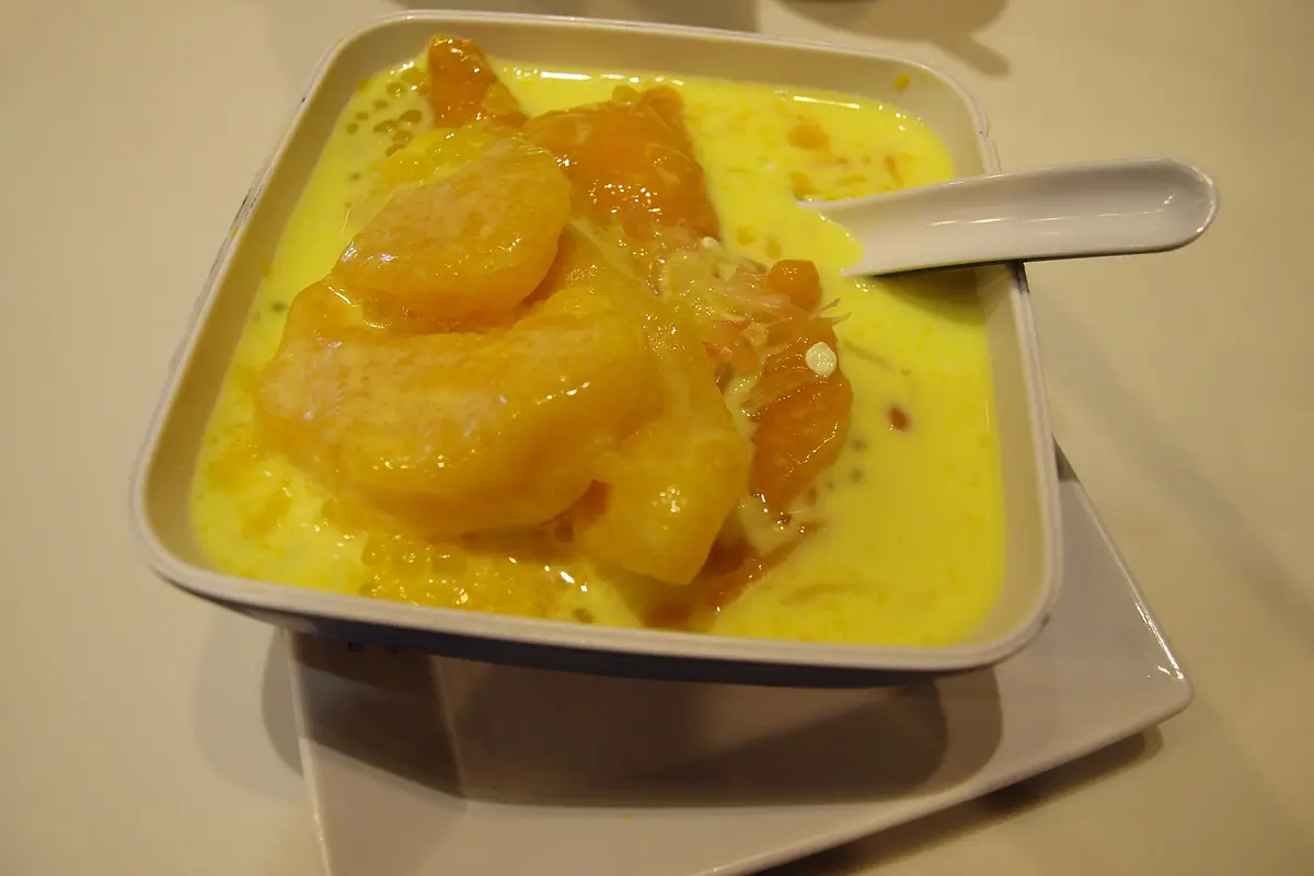 Mango pieces over shaved ice with yellow sauce and a white spoon