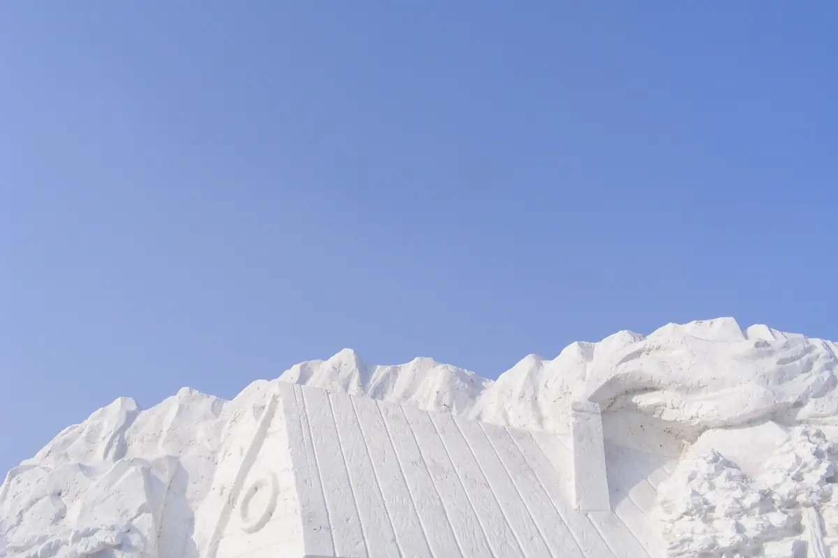 Large white ice sculpture with jagged peaks beneath a clear blue sky