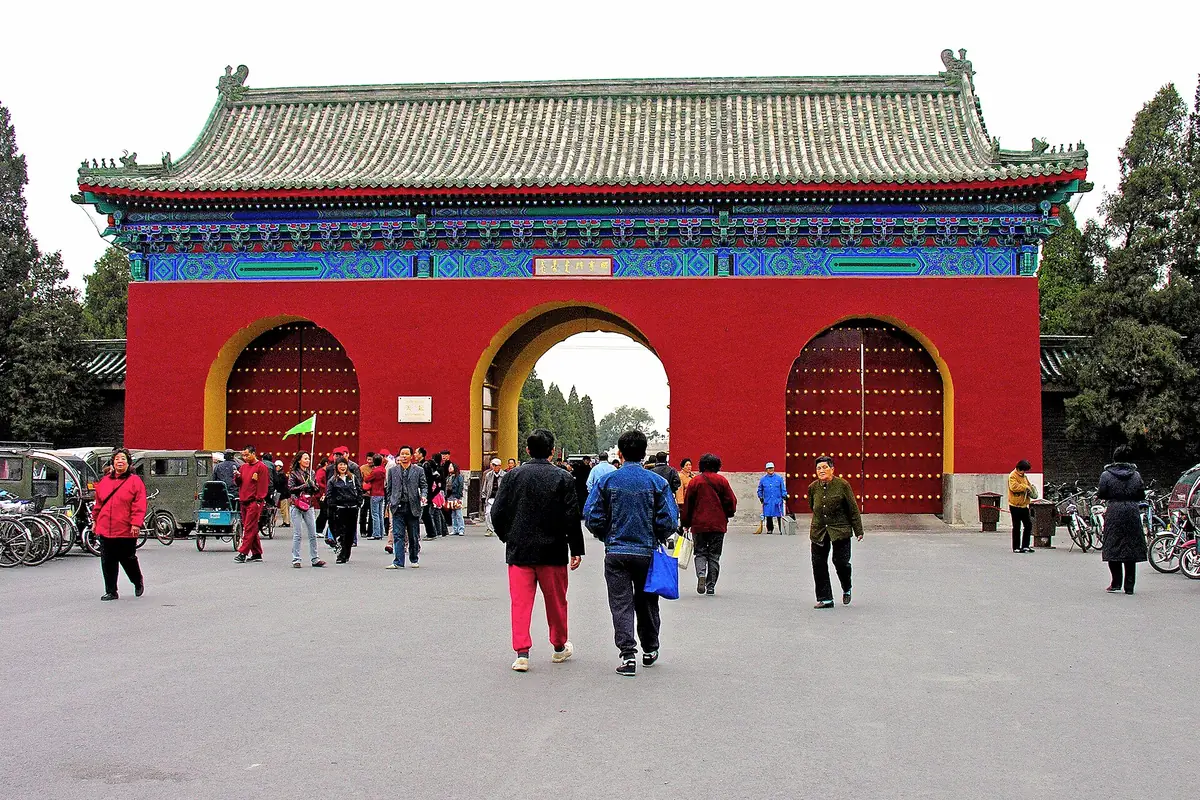 Visitors outside a red temple gateway with a green roof and colorful painted beams