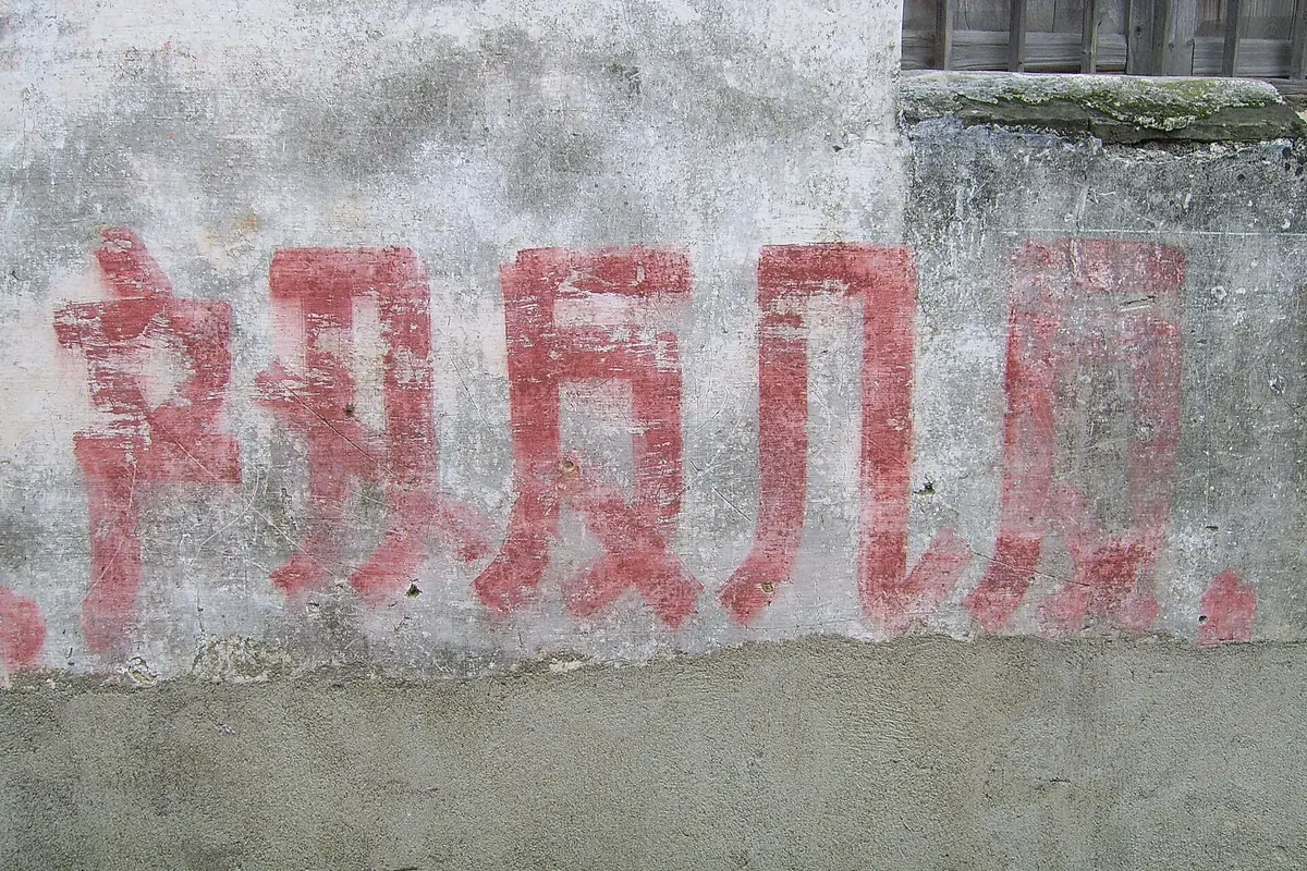 Faded red Chinese characters painted on a weathered gray wall