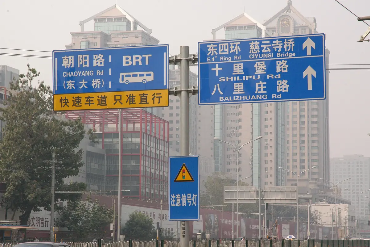 Blue-and-yellow Chinese road signs above a hazy city street