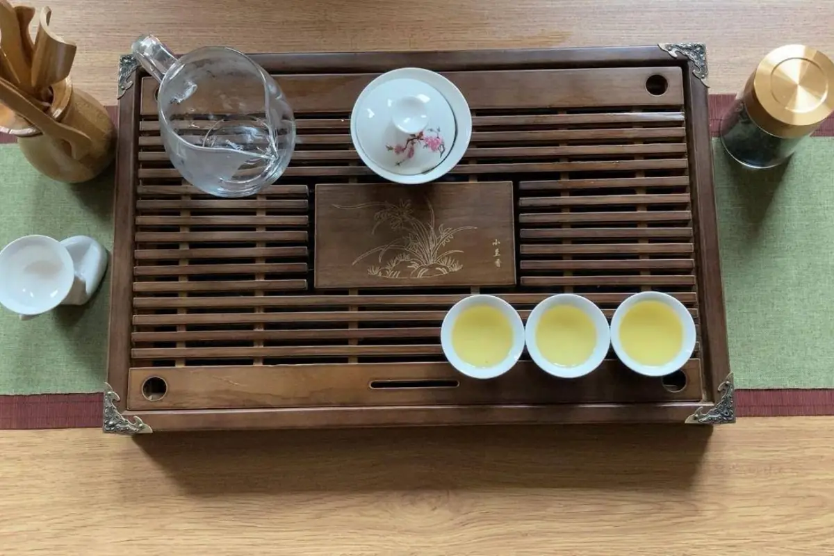 Kleine Teetassen und eine Glaskanne auf einem hölzernen Teetablett