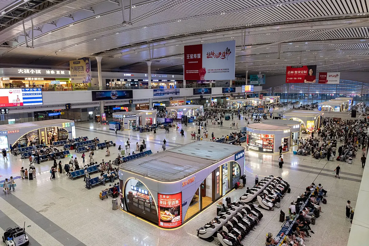Belebte Wartehalle im Terminal mit Sitzreihen und Informationsanzeigen über den Köpfen