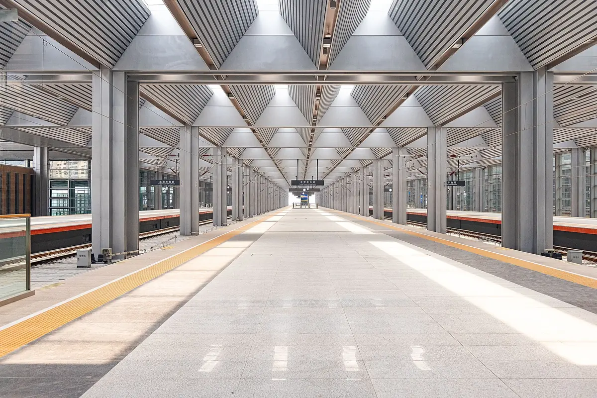 Long empty platform with yellow tactile strips beneath geometric roof beams