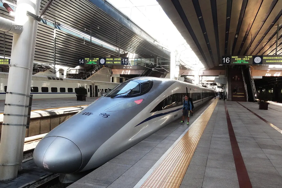 Silver high-speed train beside platform signs beneath a broad station canopy