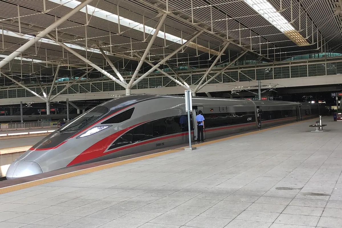 Rot-silberner Hochgeschwindigkeitszug neben einem leeren Bahnsteig unter Stahlträgern des Bahnhofsdachs