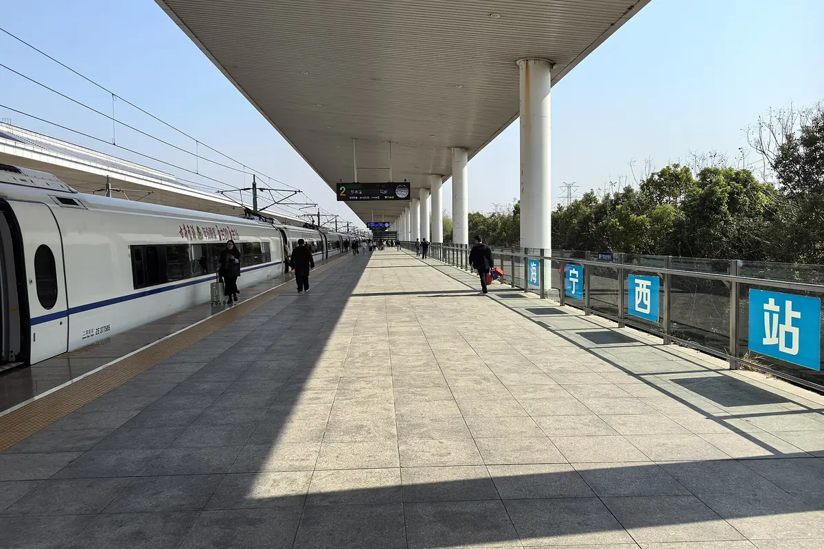 Langer weißer Zug neben einem sonnigen Bahnsteig mit blauen chinesischen Bahnhofsschildern