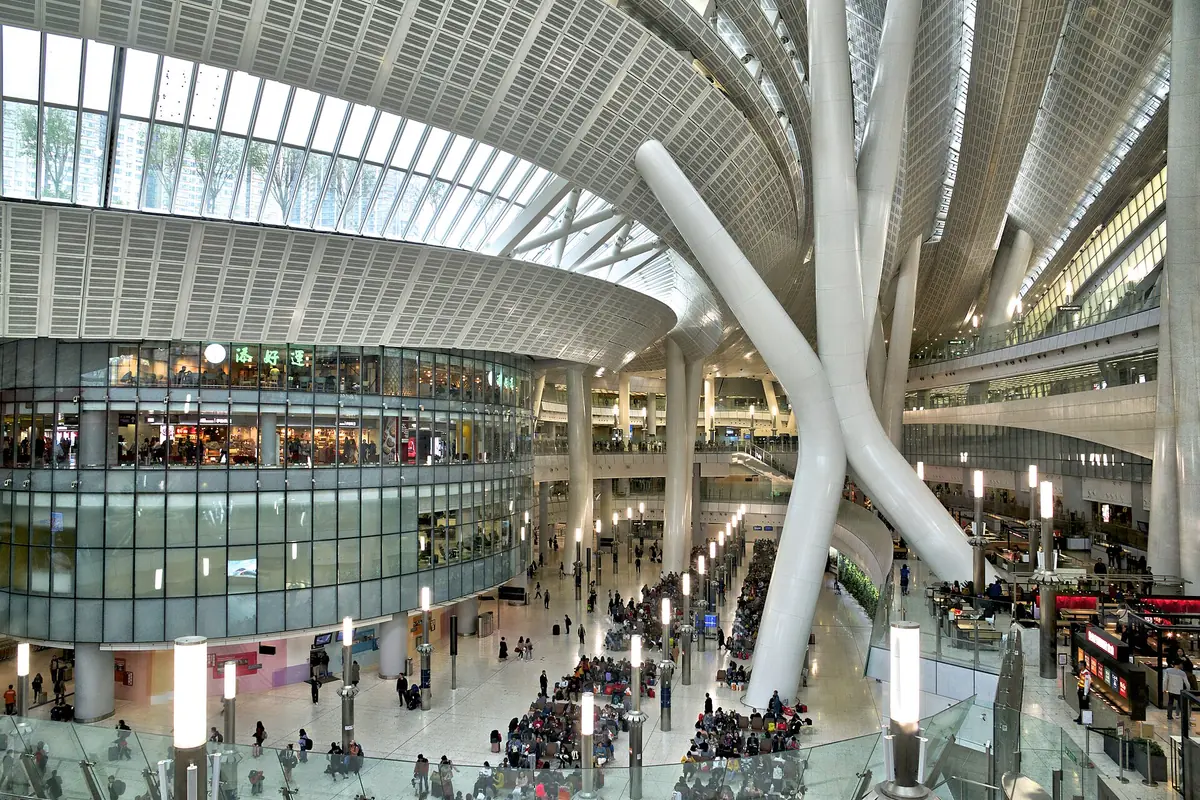 Crowded station atrium with branching white columns beneath a curved glass roof