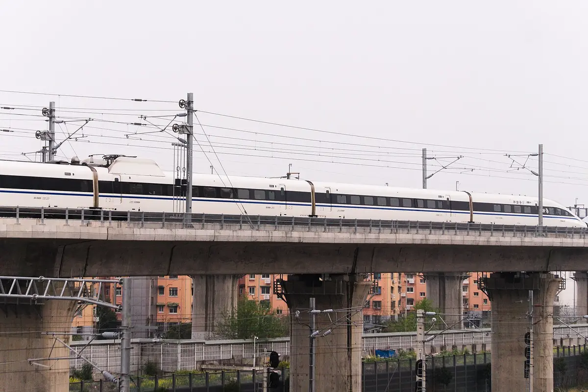 White passenger train crossing an elevated viaduct above city apartment buildings