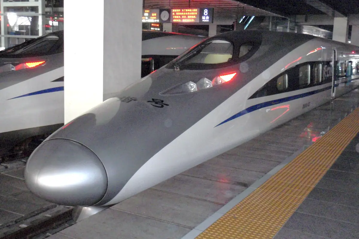 Silver high-speed train with red lights beside an indoor station platform