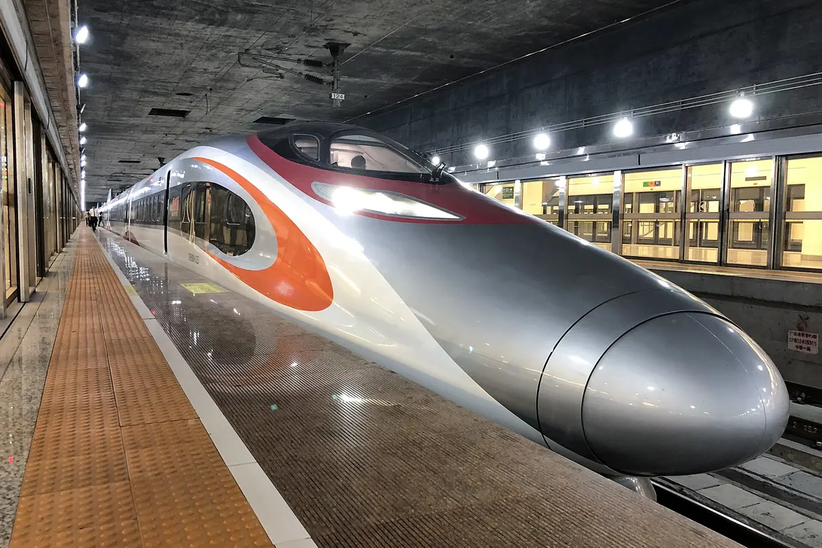 Silver high-speed train with orange trim beside a brightly lit indoor platform