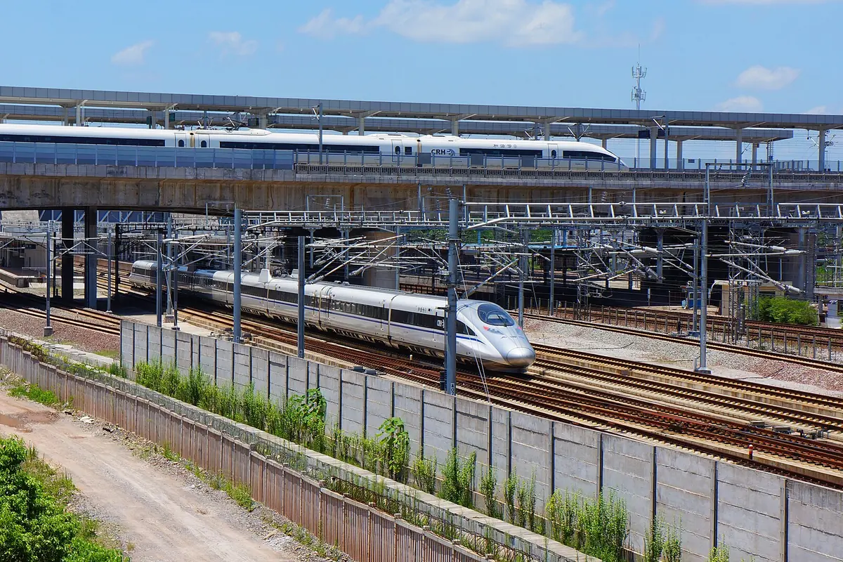 High-speed train on parallel tracks beneath elevated railway platforms