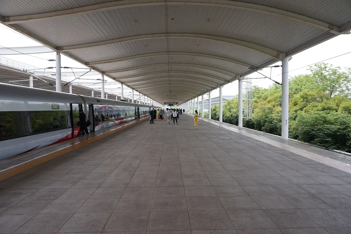 Long quai sous un toit métallique incurvé, à côté d’un train de voyageurs blanc