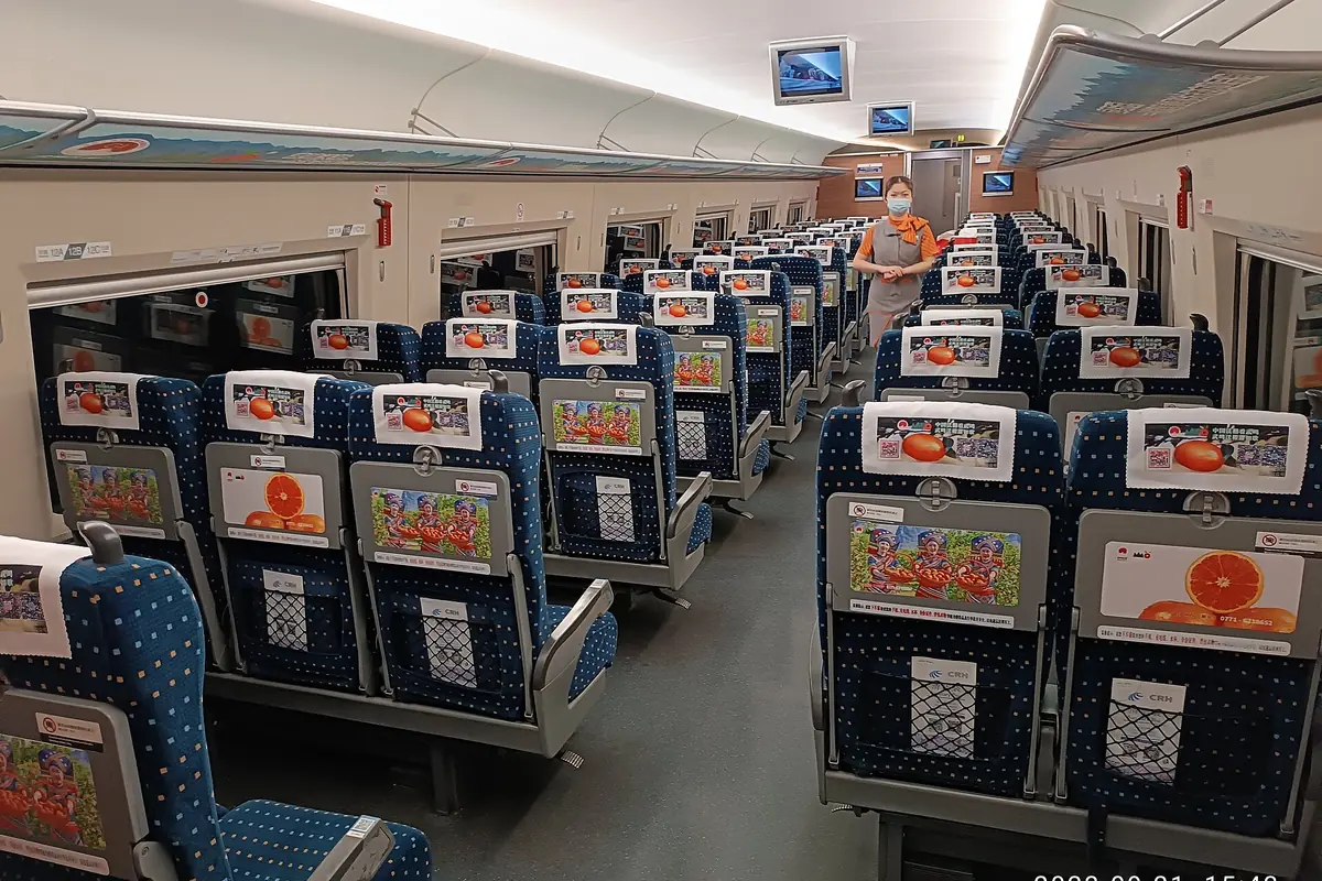 Rows of blue train seats beneath luggage racks and an onboard screen