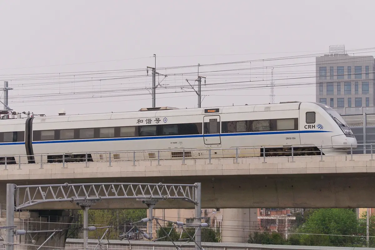 White high-speed train crossing a viaduct beneath railway wires