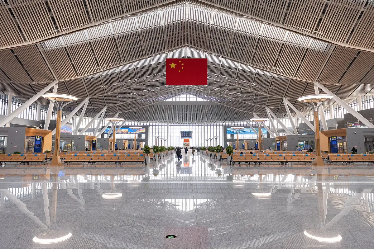 Spacious railway hall with a reflective floor beneath white roof trusses