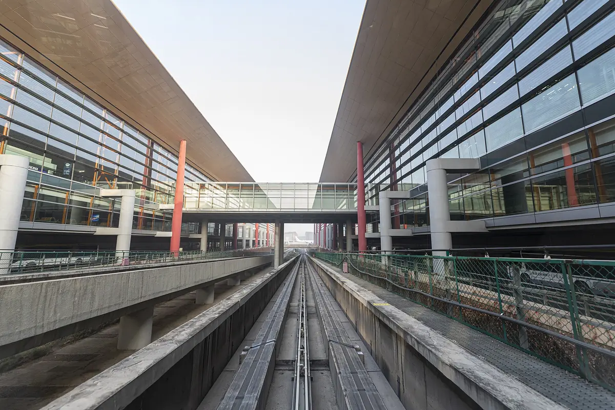 Elevated airport shuttle tracks running between glass buildings beneath a connecting roof