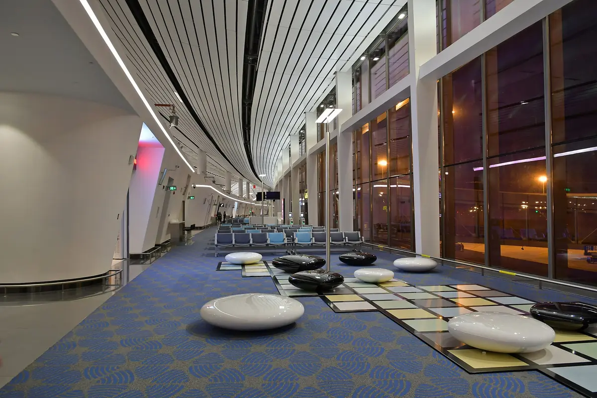 Airport waiting area with round white seats beside tall windows at night