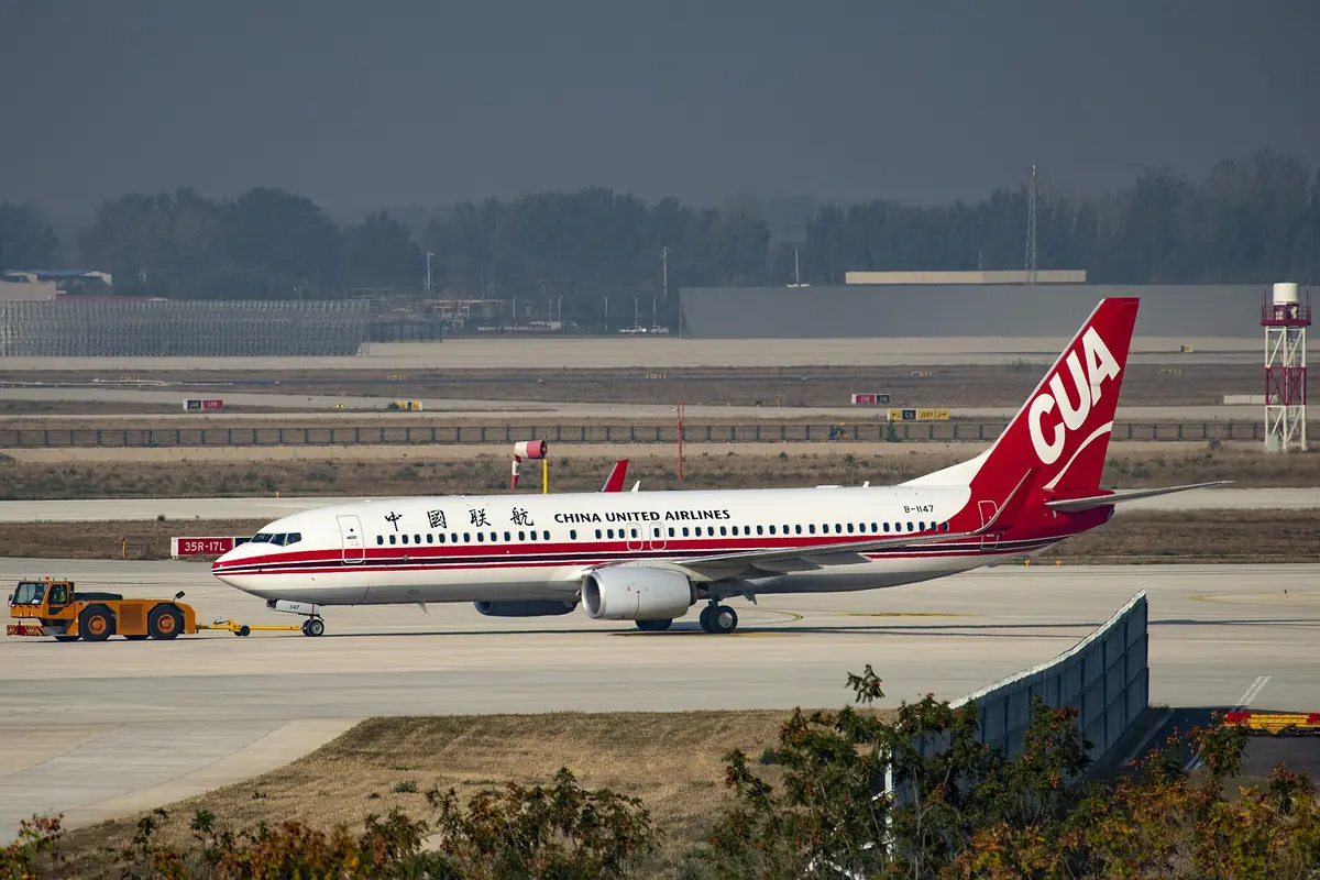 White passenger jet with a red tail taxiing along an airport apron