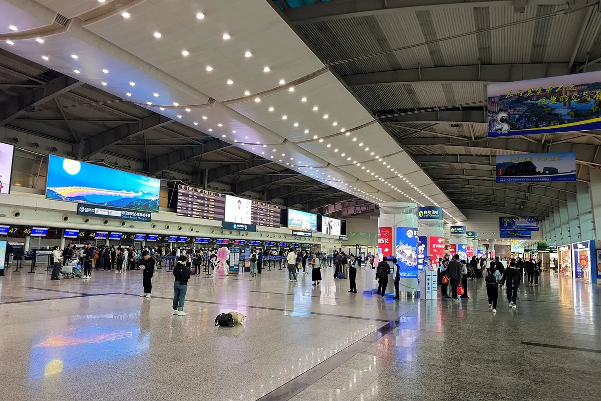 Travelers and check-in counters beneath a wide illuminated airport ceiling